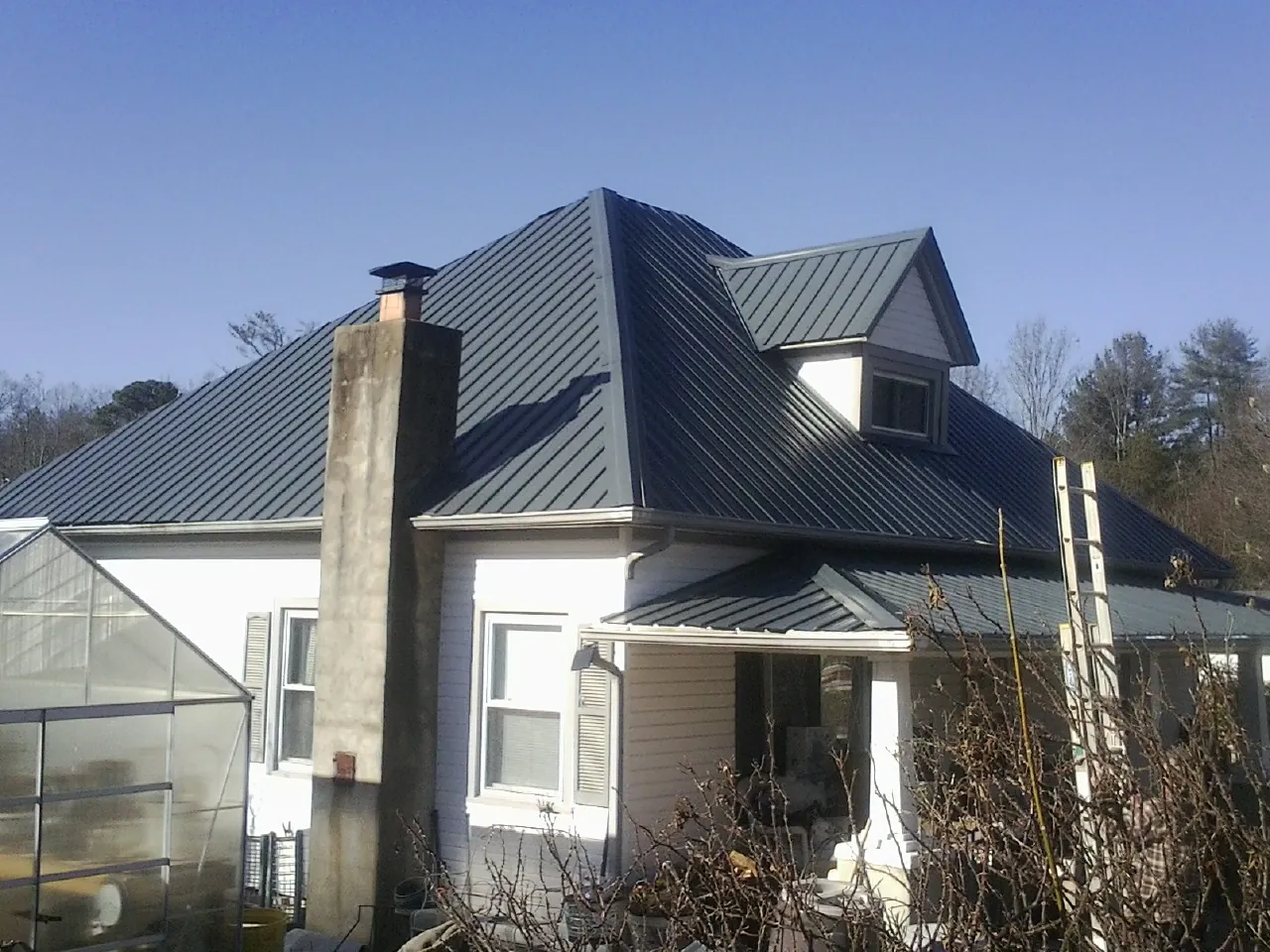 Dark blue standing seam metal roof on a white farmhouse with dormer — Slate & Tile Roof Repair by Roofing Brothers in Firth